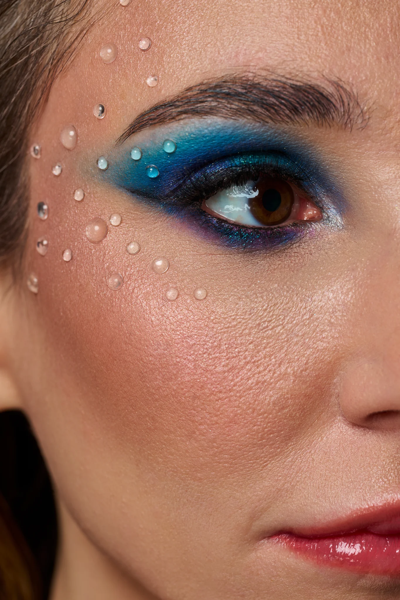 Macro close-up of blue editorial eye makeup with crystal droplets on skin, studio beauty photography Warsaw