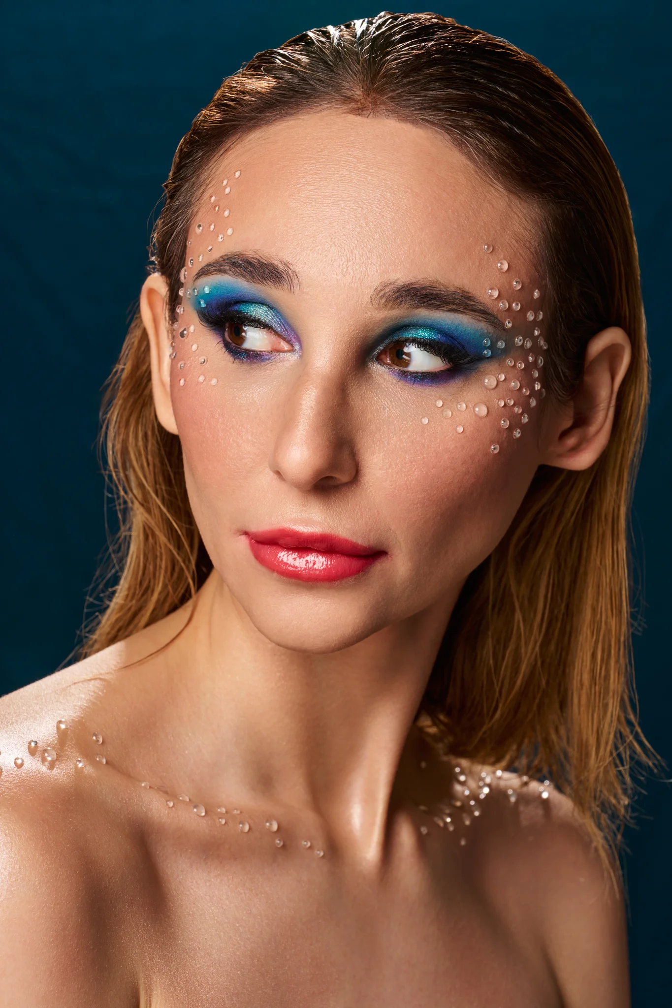 Beauty photography portrait with deep blue eyeshadow and scattered crystals on face, wet hair, off-camera gaze