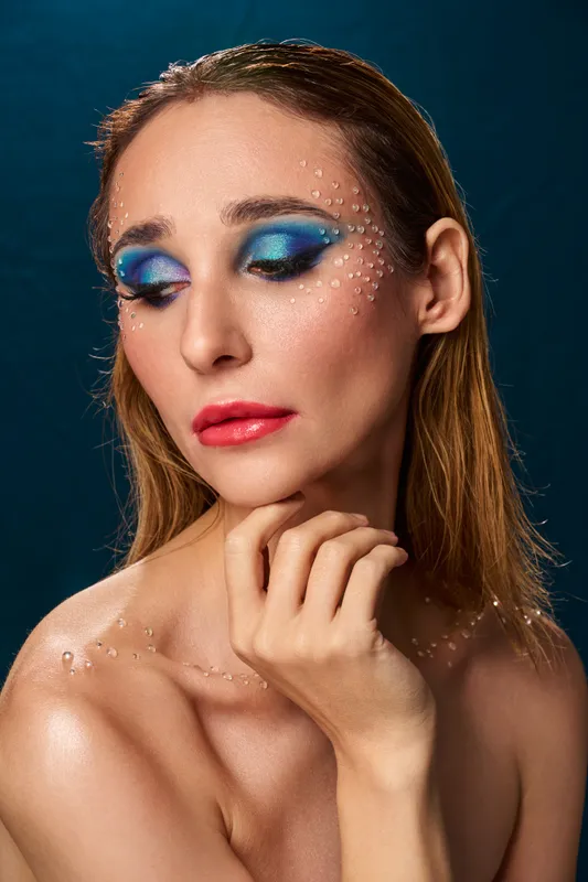 tudio editorial beauty portrait with blue eye makeup, crystal accents on face and shoulders, hand at chin, Warsaw